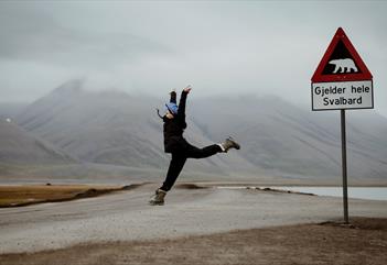 Person jumping in a split, in front of the polar bear road sign, with cloudy mountains in the background