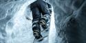 A person wearing snowmobile equipment climbing down a ladder into an ice cave