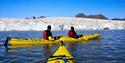 Two yellow kayaks in front of a glacier. Two persons are sitting in one of the kayaks