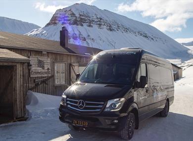 A minibus parked in front of a building with snow-covered mountains in the background