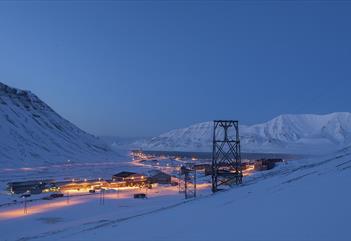 Landscape photo of Longyearbyen seen from above in blue winter light with snow-covered mountains in the background