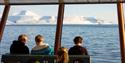 Guests sitting inside MS Bard with a fjord and mountains in the background
