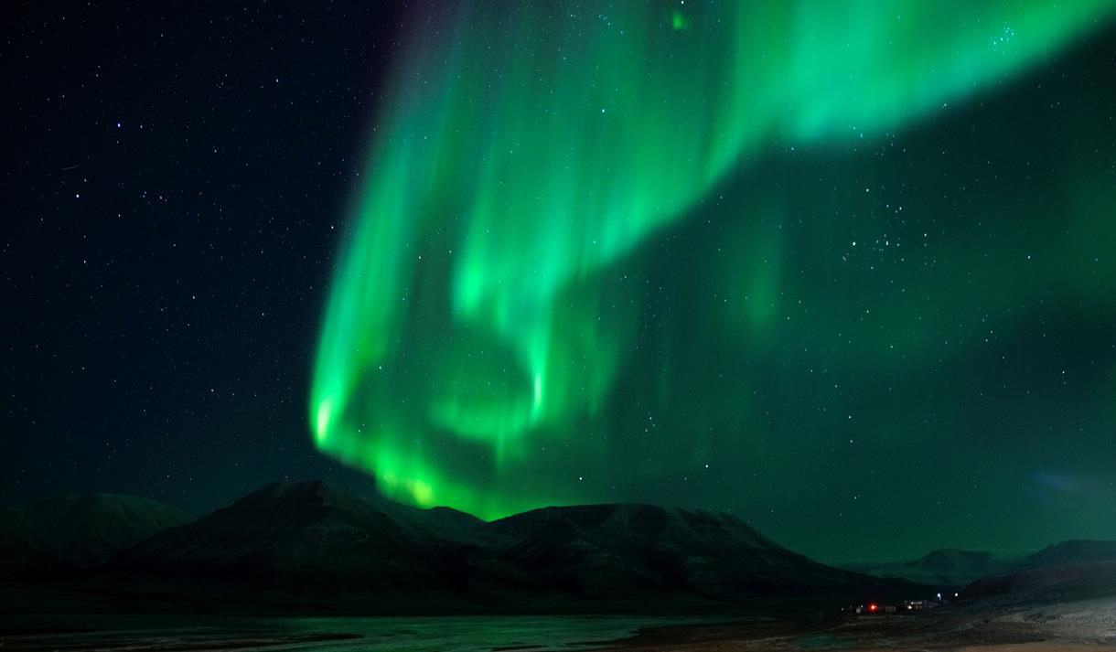 Northern lights shining in the skies with dark mountains in the background