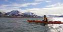 A person in a kayak on a fjord with mountains in the background