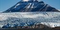 Et stort fjell som stikker opp fra en isbre med en fjord i forgrunnen