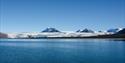 En åpen og rolig blå fjord med fjell og en stor isbre i bakgrunnen