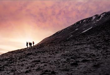 En gruppe med personer som står på en fjellrygg i silhuett mot en lys himmel i bakgrunnen