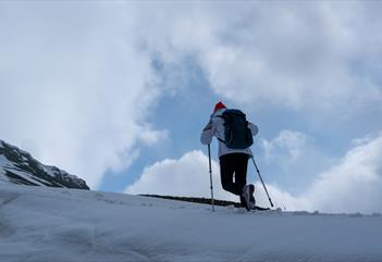 En person som går til fots opp en fjellrygg med staver