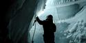 A person wearing snowmobile equipment holding a rope inside a dark ice cave