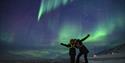 To personer poserer sammen for kamera under nordlyset på himmelen