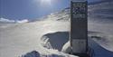 The entrance to Svalbard Global Seed Vault in bright snowy surroundings with sunshine and a blue sky in the background