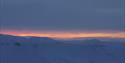 A snow-covered landscape with low clouds and a thin stripe of light from a sunset far in the background