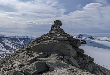 En fjellrygg med formasjonen kjent som Trollsteinen på toppen, med lett snødekte fjell og en skyet himmel i bakgrunnen