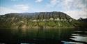 A green mountain landscape along the edge of a calm fjord