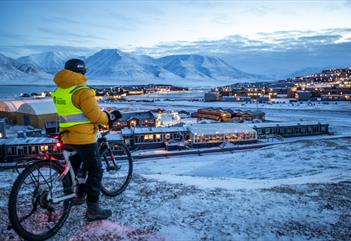 En gjest på sykkel som ser ut over bygningene i Longyearbyen fra et utsiktspunkt