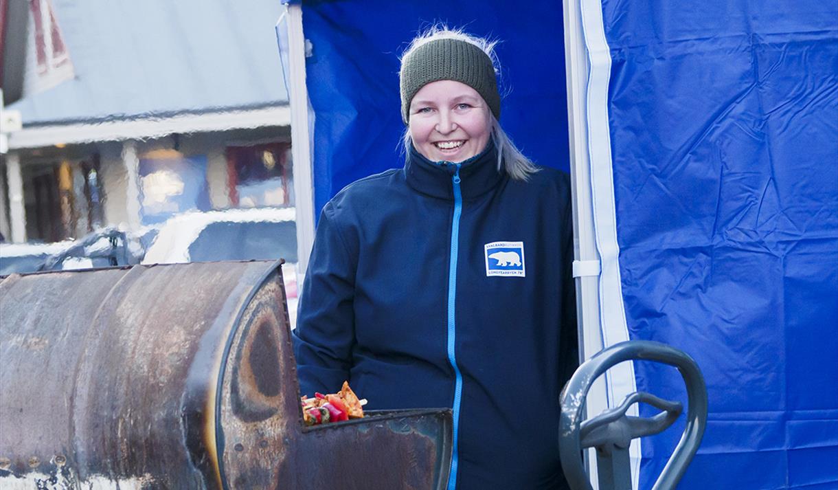 En ansatt fra Coop Svalbard som står i et blått telt og griller mat