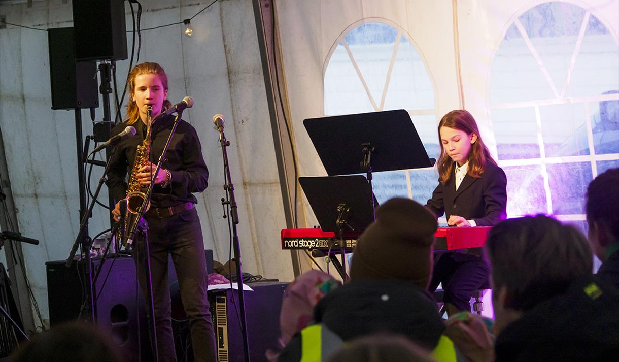 Two students from Longyearbyen's cultural school playing the saxophone and keyboard in front of a crowd in Taste Svalbard's festival tent