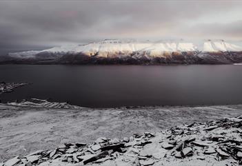 En snødekt steinrøys i forgrunnen med en fjord og snødekte fjell i bakgrunnen