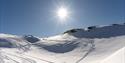 Et snødekt bre- og morenelandskap med personer i det fjerne som går på ski opp mot en fjelltopp i bakgrunnen