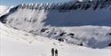 To personer som på fottur i et snødekt landskap på en isbre, med en morene og et fjell i bakgrunnen