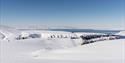 Et snødekt fjellandskap med en fjord og en skyfri blå himmel i bakgrunnen