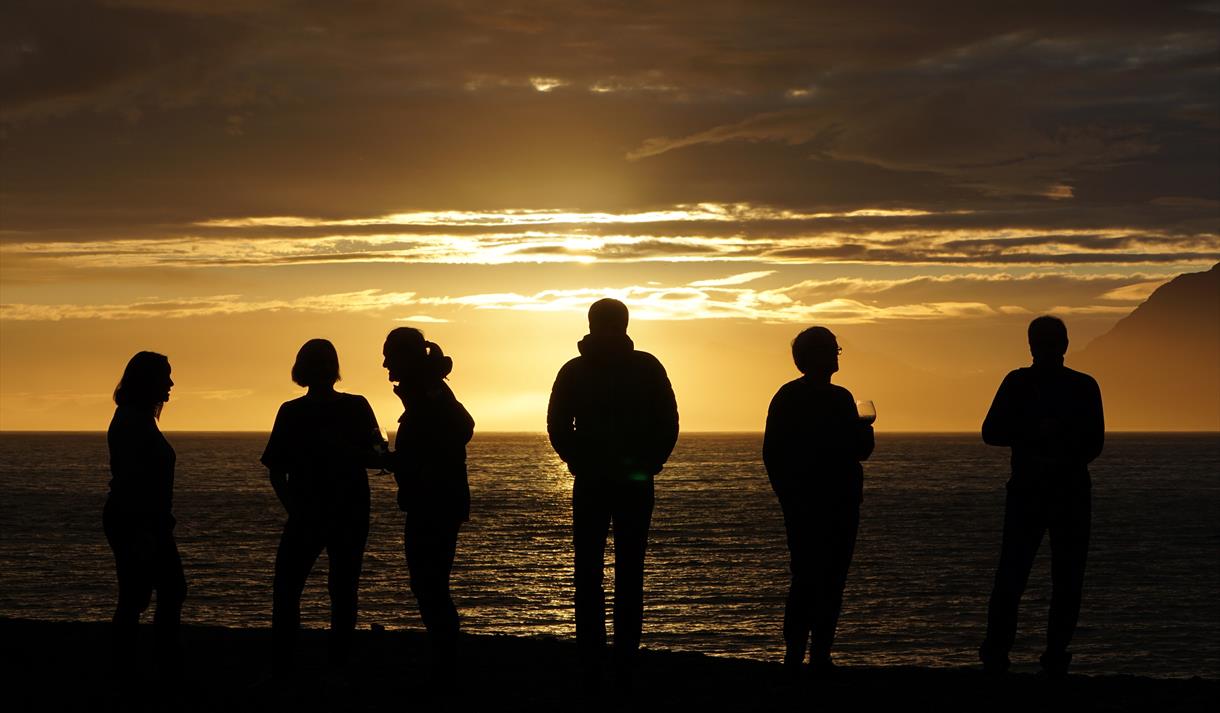 Persons in silhouette against the sun looking out over a fjord