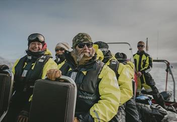 Glade gjester som sitter om bord en RIB båt på tur, iført redningsvester og flytedresser