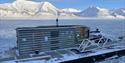 The sauna SvalBad floating in the port of Longyearbyen with snow-covered mountains and a fjord with drift ice in the background