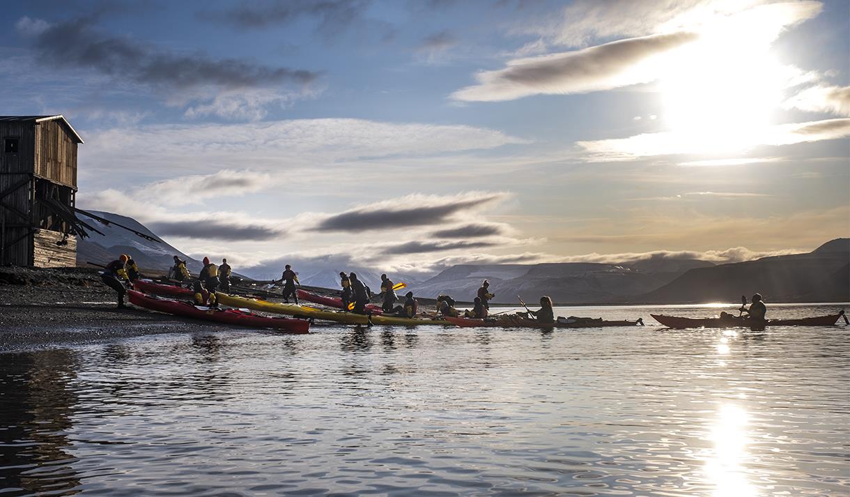 A group of guests and guides pulling kayaks on shore with sunshine and a partially clouded sky in the background