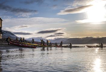 A group of guests and guides pulling kayaks on shore with sunshine and a partially clouded sky in the background