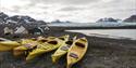Kayaks laid on shore next to a tent camp in the foreground, with a fjord, a glacier and mountains in the background