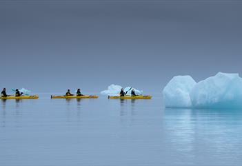 Three kayaks with guests paddling between nearby floating icebergs