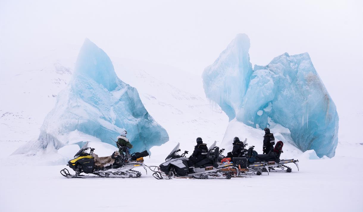 A guide and guests with snowmobile taking a break next to two large icebergs frozen in sea ice