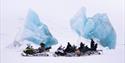 A guide and guests with snowmobile taking a break next to two large icebergs frozen in sea ice