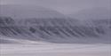 En guide og gjester på snøscootere i et landskap med fjell i bakgrunnen