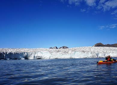 A person sitting in a kayak in front of a glacier 
