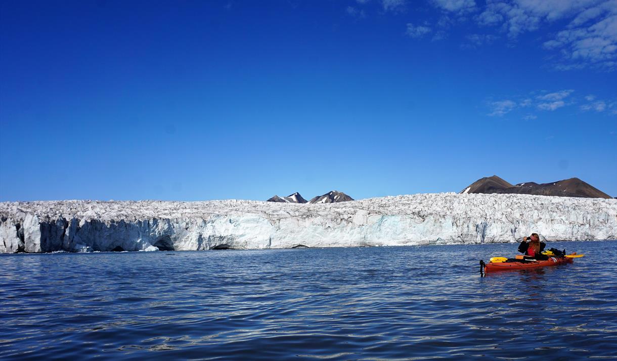 A person sitting in a kayak in front of a glacier