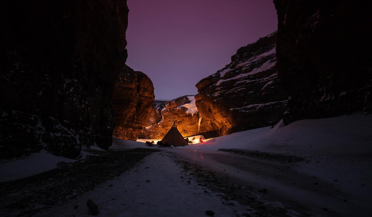 A tent is set up in a narrow valley. The sky is purple.