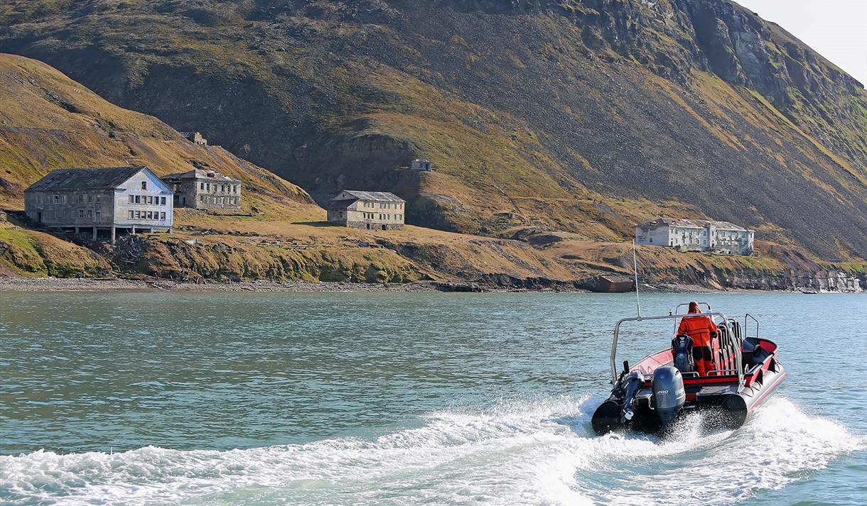 En guide som seiler en RIB båt mot den forlatte bosetningen Grumant langs Isfjorden