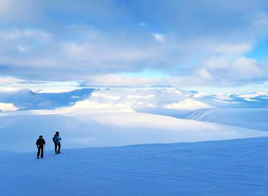 Two persons standing on a glacier looking at the view