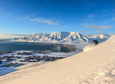 A person skiing down a mountain with Longyearbyen and a mountainous landscape in the background