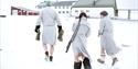 Three guests in bathrobes and winter boots on their way from a sauna to the main building at Isfjord Radio. One guest is carrying a rifle.