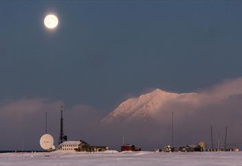 Isfjord Radio i vinterlandskap med tåke over fjorden i bakgrunnen og månen som skinner på himmelen.