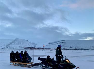 A guide driving a snowmobile with guests on the sled being pulled behind