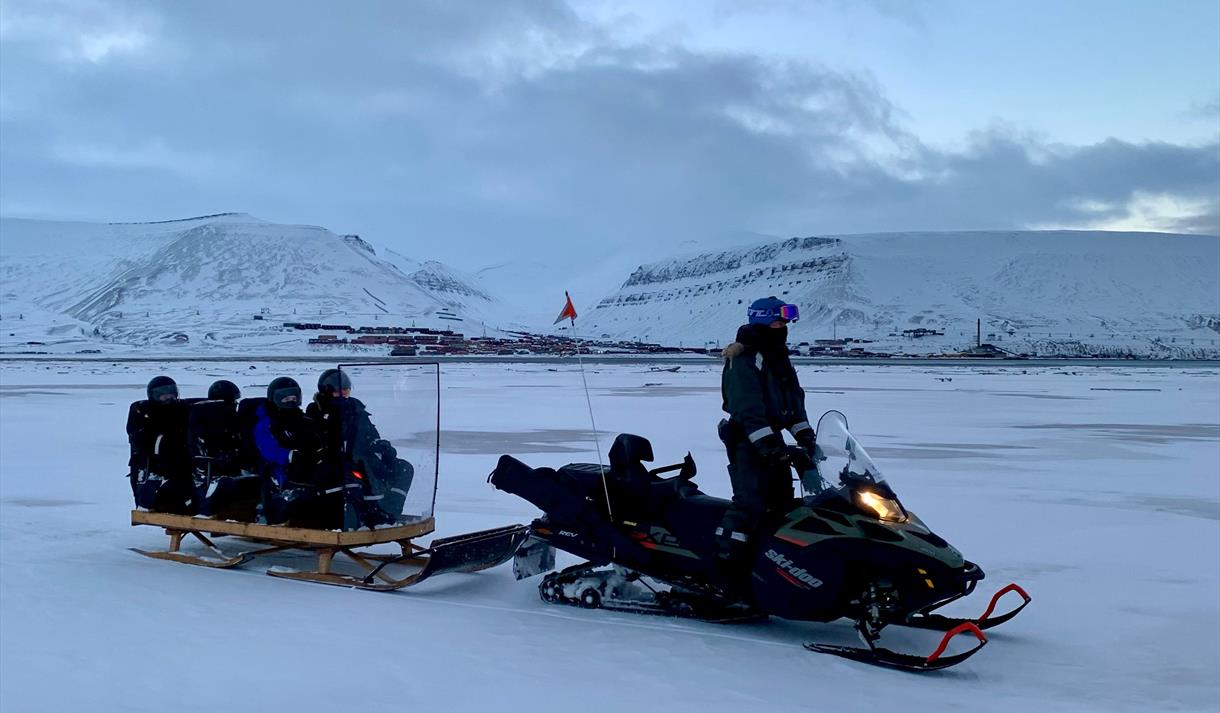 A guide driving a snowmobile with guests on the sled being pulled behind