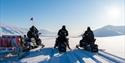 En guide og to gjester på snøscootere som ser utover et snødekt landskap i bakgrunnen.