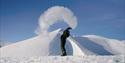En guide i snøscooterutstyr som kaster kokende vann i luften slik at det fordamper i vinterkulda. I bakgrunnen ligger det et snødekt fjellandskap.