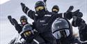 A group of guests in snowmobile equipment cheering in front of the camera.