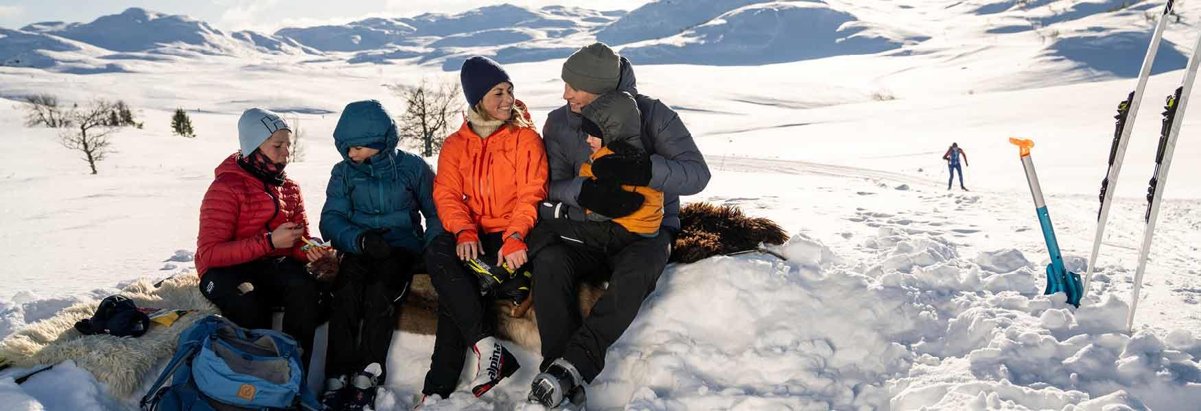 familie på 4 sitter i snøen i påskeferie