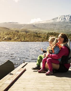 Mor og datter sitter ved innsjøen foran Gaustatoppen i Telemark